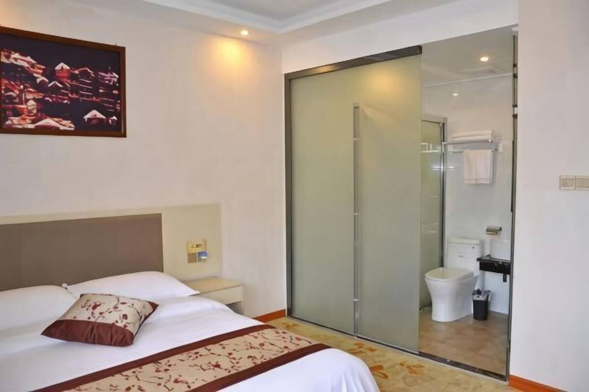 A hotel room with a bed, a bedside table, a shower area, and a bathroom.