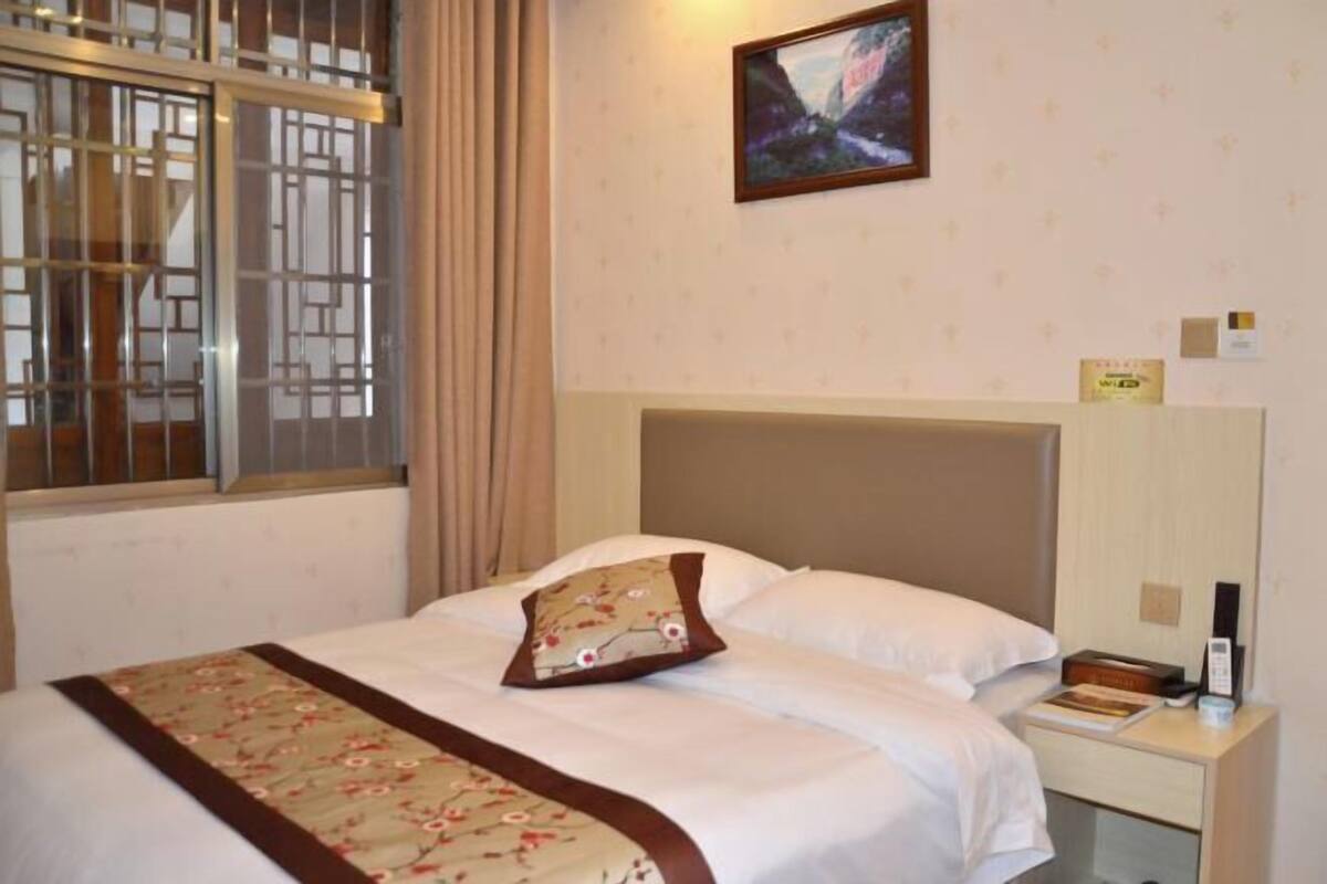 A hotel room with a bed, a nightstand, a picture on the wall, and a window with curtains.