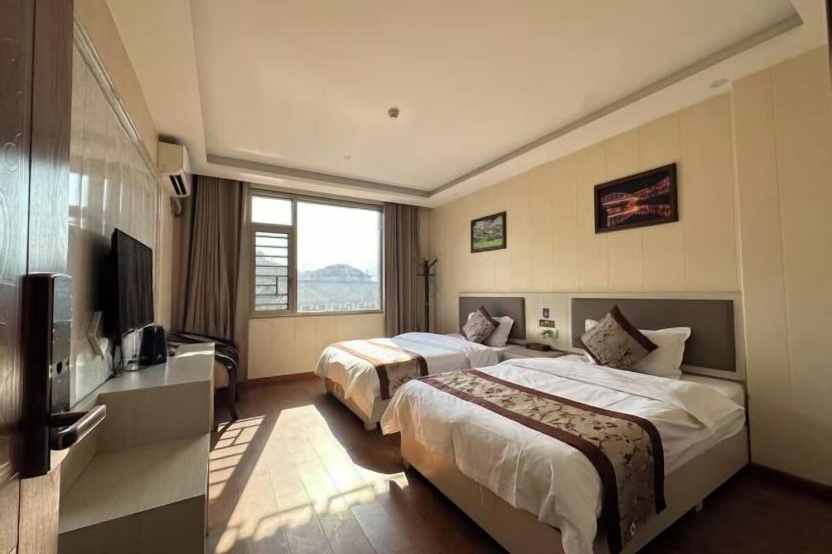 A hotel room with two beds, a desk, a TV, and a window with a view.
