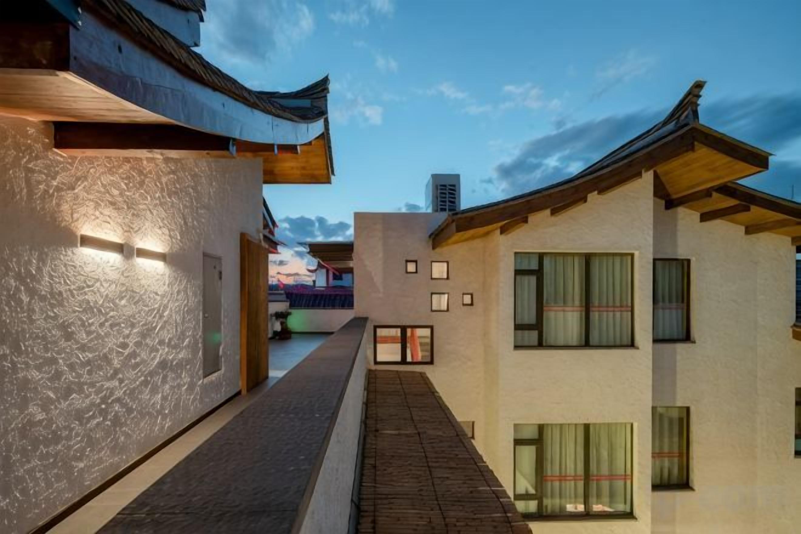 A narrow alleyway between buildings with traditional and modern architectural styles, a clear sky, and a distant mountain.