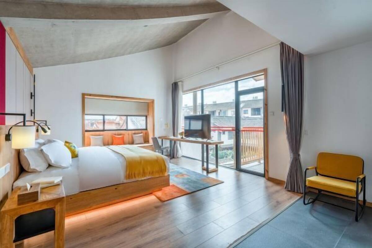 Een moderne hotelkamer met een groot bed, een bureau, een stoel, en een balkon met uitzicht op de stad.