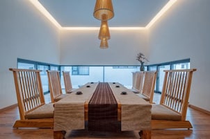 A long dining table with chairs, a hanging light fixture, and large windows.