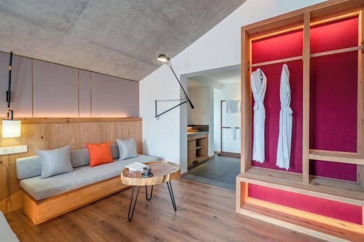 Een moderne woonkamer met een bank, een rond houten bijzettafeltje en een rode muur met badjassen.