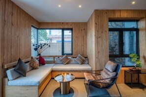 A modern interior with wooden walls, a sofa, a chair, a round table, and large windows. - Mouding Lanyun Homestay (Mouding)
