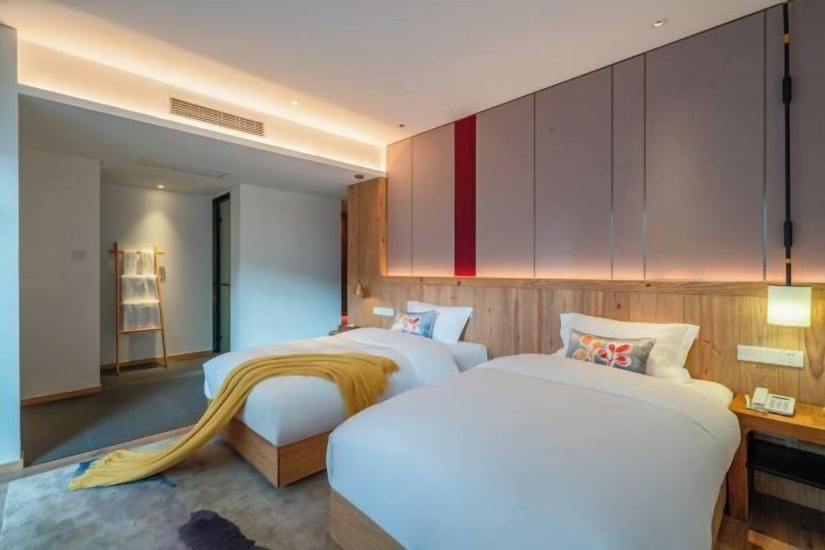Een moderne hotelkamer met twee bedden, een houten hoofdbord, een nachtkastje met een lamp en een klein bureau met telefoon.