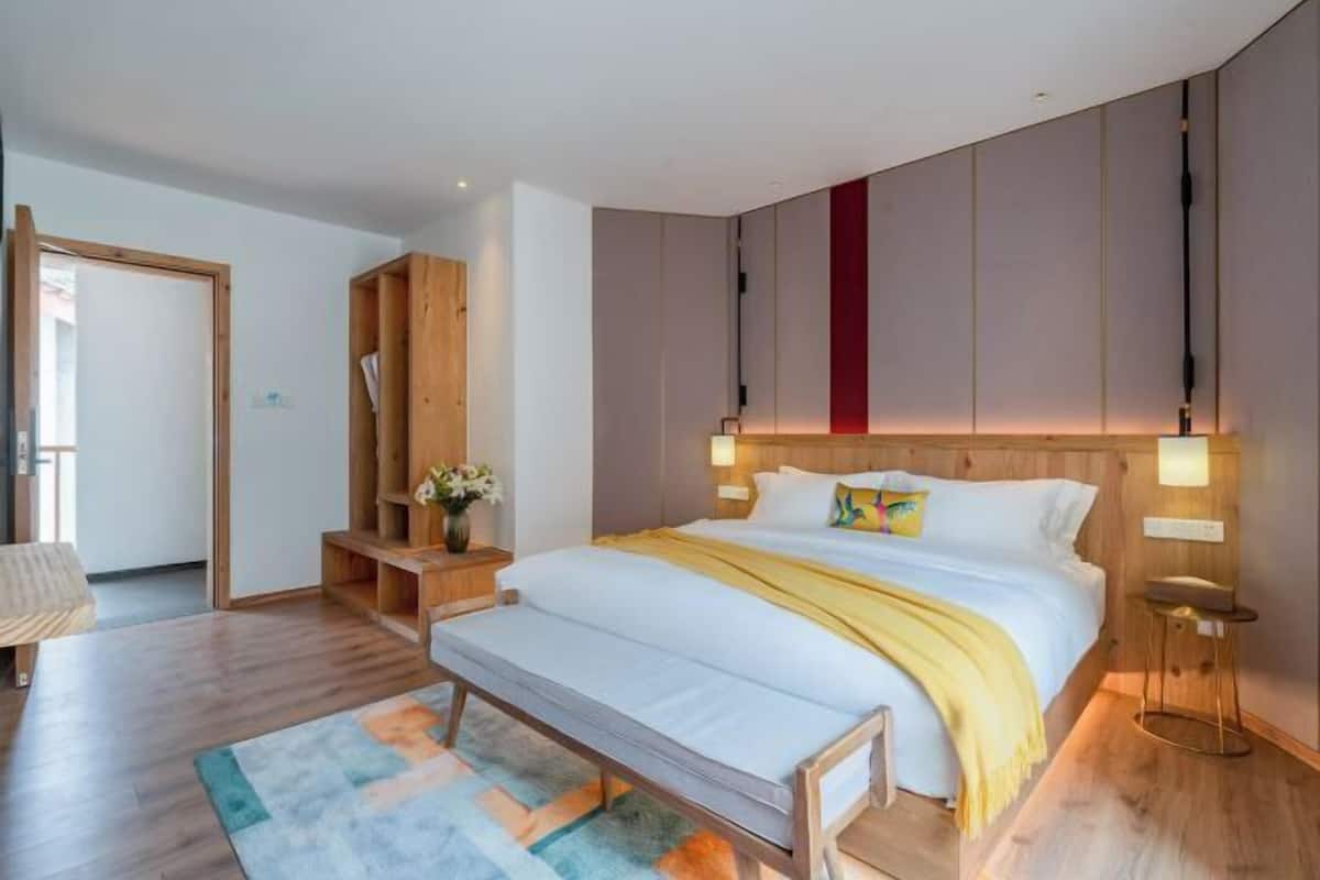 Een moderne slaapkamer met een houten hoofdbord, een nachtkastje met een lamp, een bankje en een kleurrijk vloerkleed.