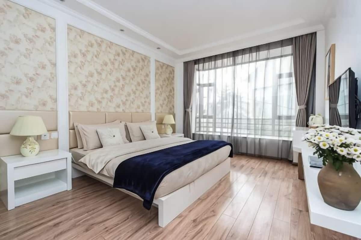 A bedroom with a bed, nightstands, a dresser, a mirror, and a window with curtains.