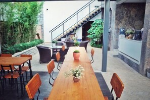 An outdoor dining area with a long wooden table, chairs, and potted plants.