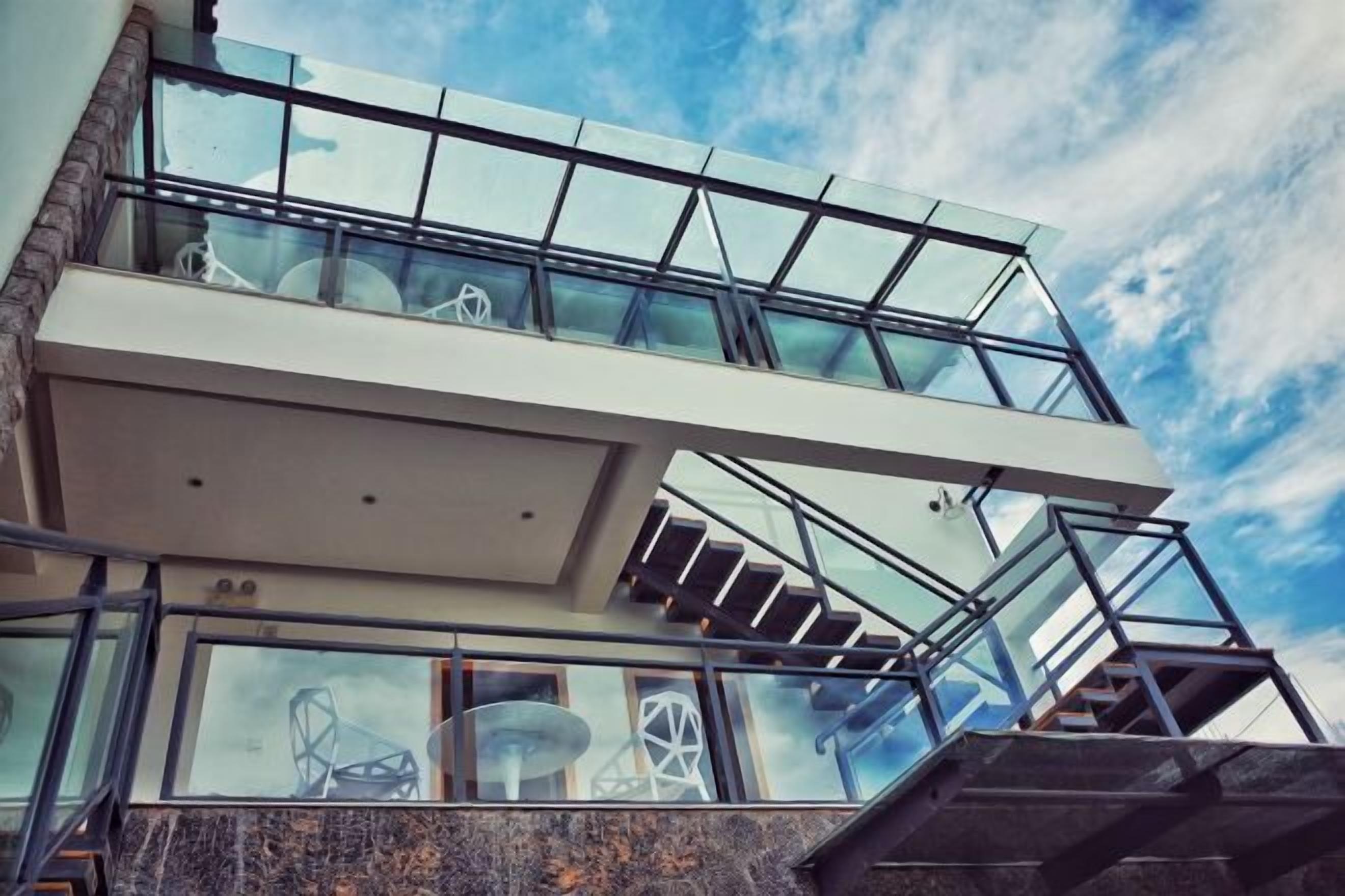 Un edificio moderno con balcón de cristal y escalera que sube a un nivel superior.