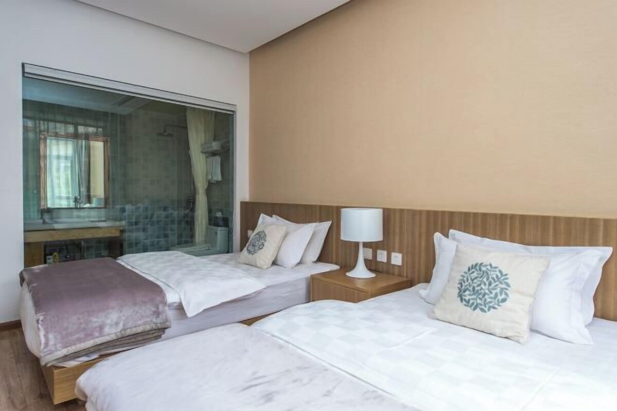 A hotel room with two beds, a nightstand with a lamp, a large mirror, and a view of a bathroom.