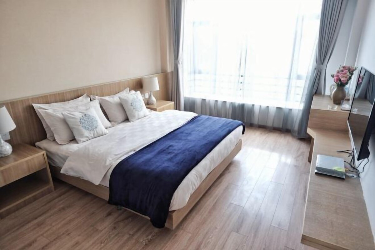 A hotel room with a bed, bedside tables, a TV, and a window with curtains.