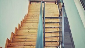 Una escalera de madera con barandillas de metal y una puerta de ascensor de vidrio.
