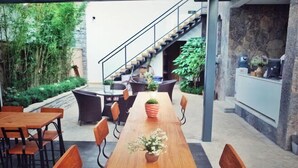 Una larga mesa de madera con sillas, rodeada de vegetación y una escalera.