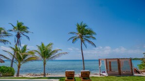Vista sulla spiaggia con palme, un gazebo in legno e due poltrone da relax.