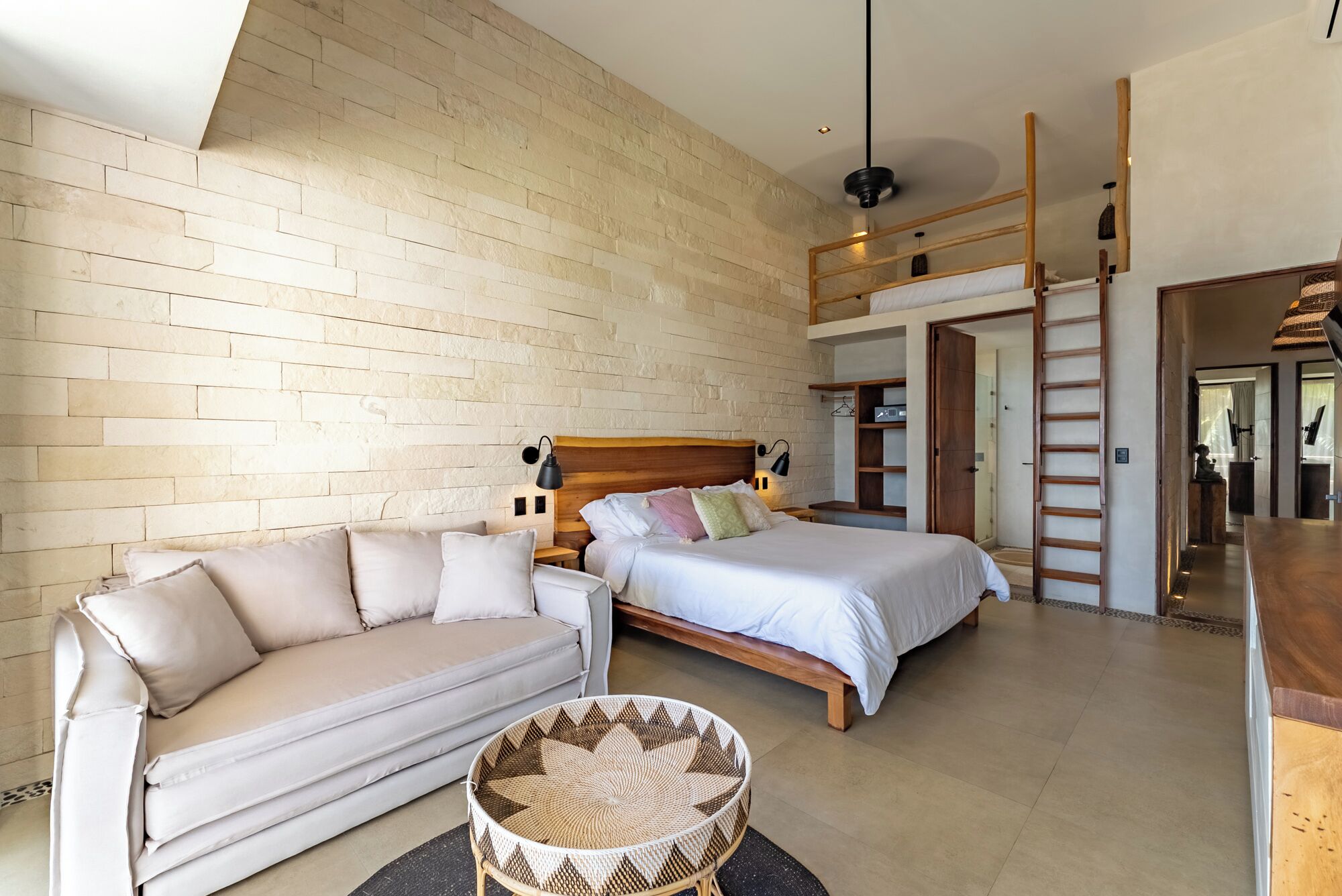 A modern bedroom with a sofa, two beds, a ladder, and a hanging light fixture.