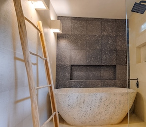 Un baño moderno con una bañera independiente, una escalera de madera y una pared de piedra con un espacio empotrado.
