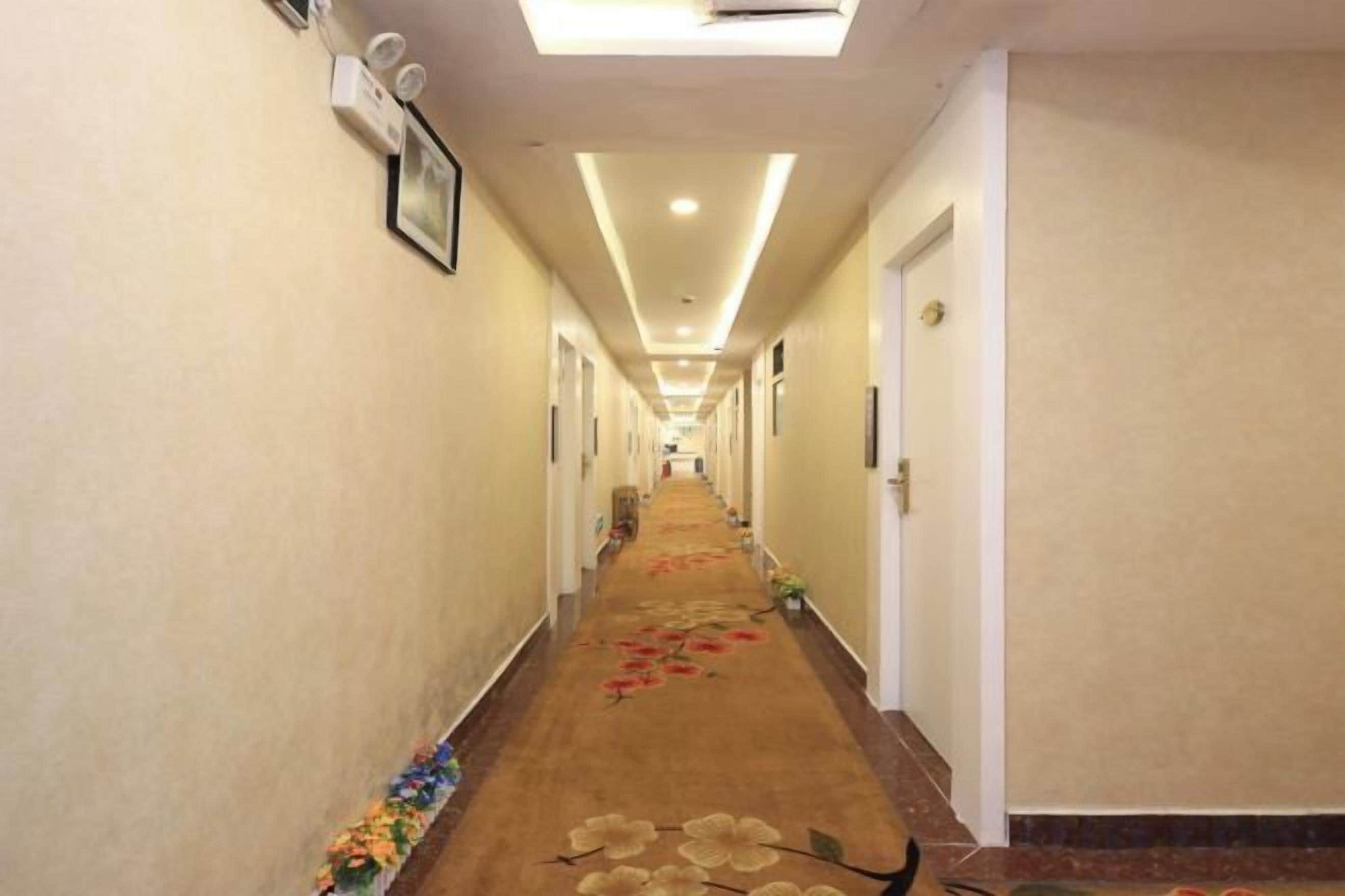 Corredor de hotel com piso coberto de carpete, portas em ambos os lados e luminária no teto.