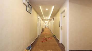 Corredor de hotel com piso coberto de carpete, portas em ambos os lados e luminária no teto.