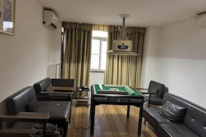 Una habitación con mesa de billar, dos sofás, una lámpara de techo y un ventanal con cortinas.