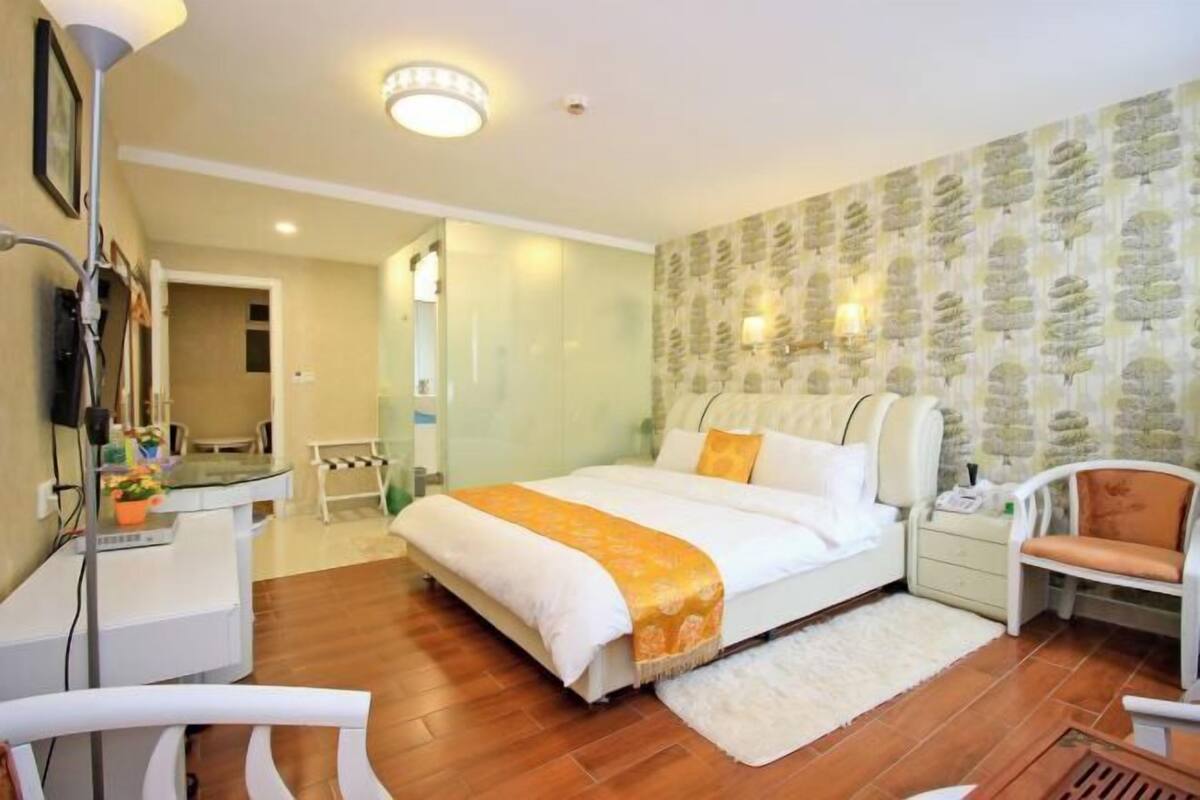 Un dormitorio con cama, mesita de noche, silla y escritorio con lámpara.