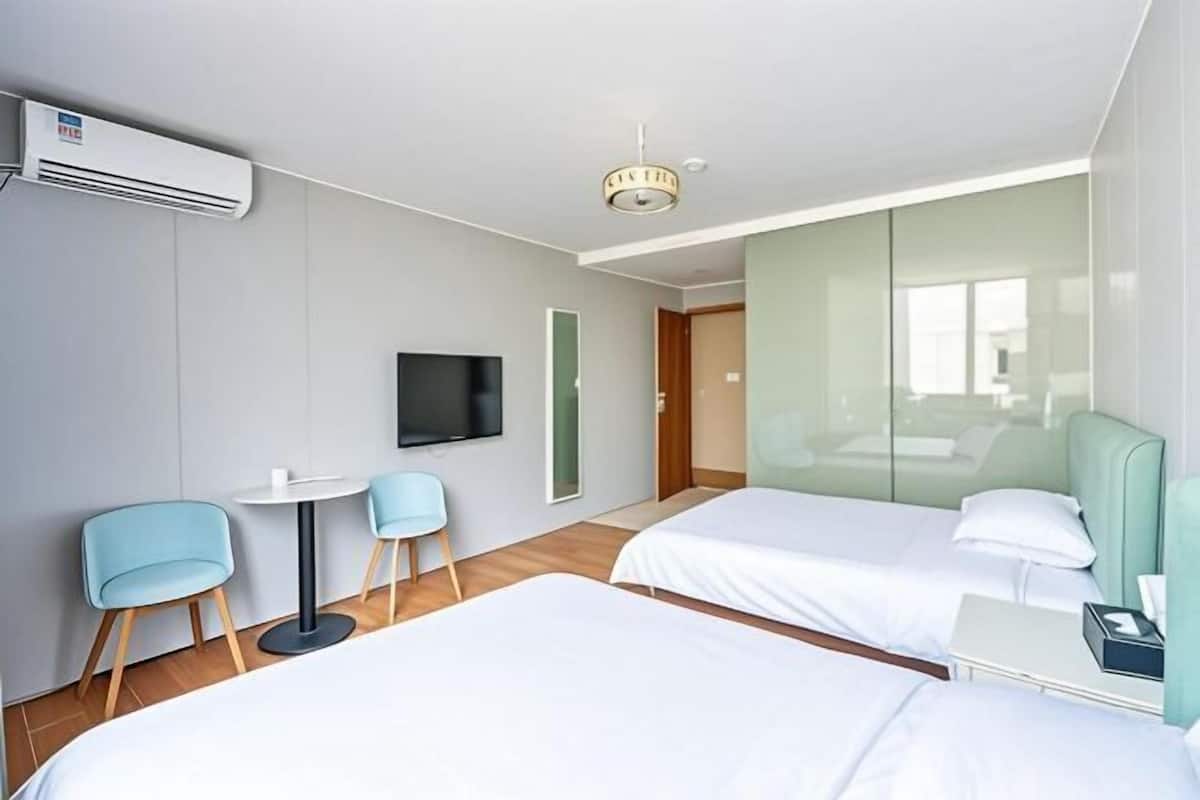 Habitación de hotel con dos camas, televisor, una mesita y una silla.