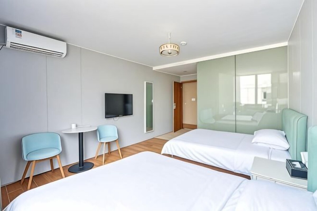 A hotel room with two beds, a TV, a small table, and chairs.