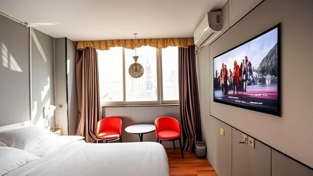 A hotel room with a bed, two red chairs, a small table, a TV on the wall, and a window with curtains. - Shenzhen Huashang Hotel (Hongling Subway Station KKmall) (Shenzhen)