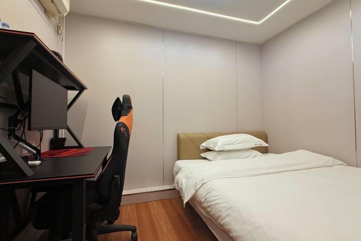 A compact hotel room with a single bed, a desk with a computer, and a chair.