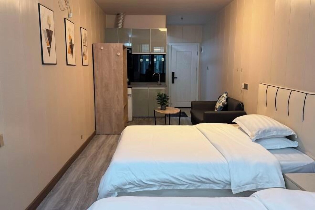 A hotel room with a bed, a small table, and a kitchenette in the background.