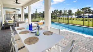 A covered outdoor dining area with a pool view, white table, and chairs.