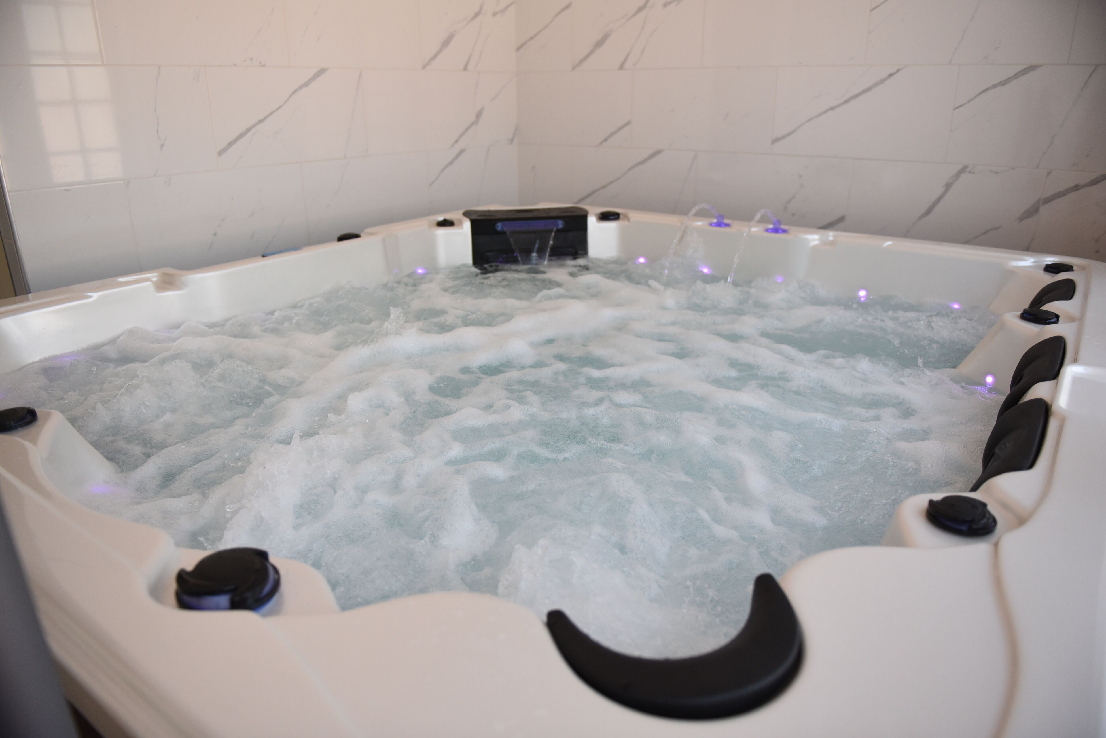 A hot tub with water jets and control buttons, surrounded by white marble tiles.