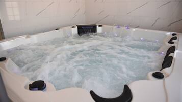 A hot tub with water jets and control buttons, surrounded by white marble tiles.