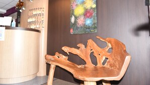 A wooden reception desk with a chair in front, a wall-mounted key display, and a colorful artwork. - Hotel Le Normandie Spa (Bagnoles-de-l'Orne)