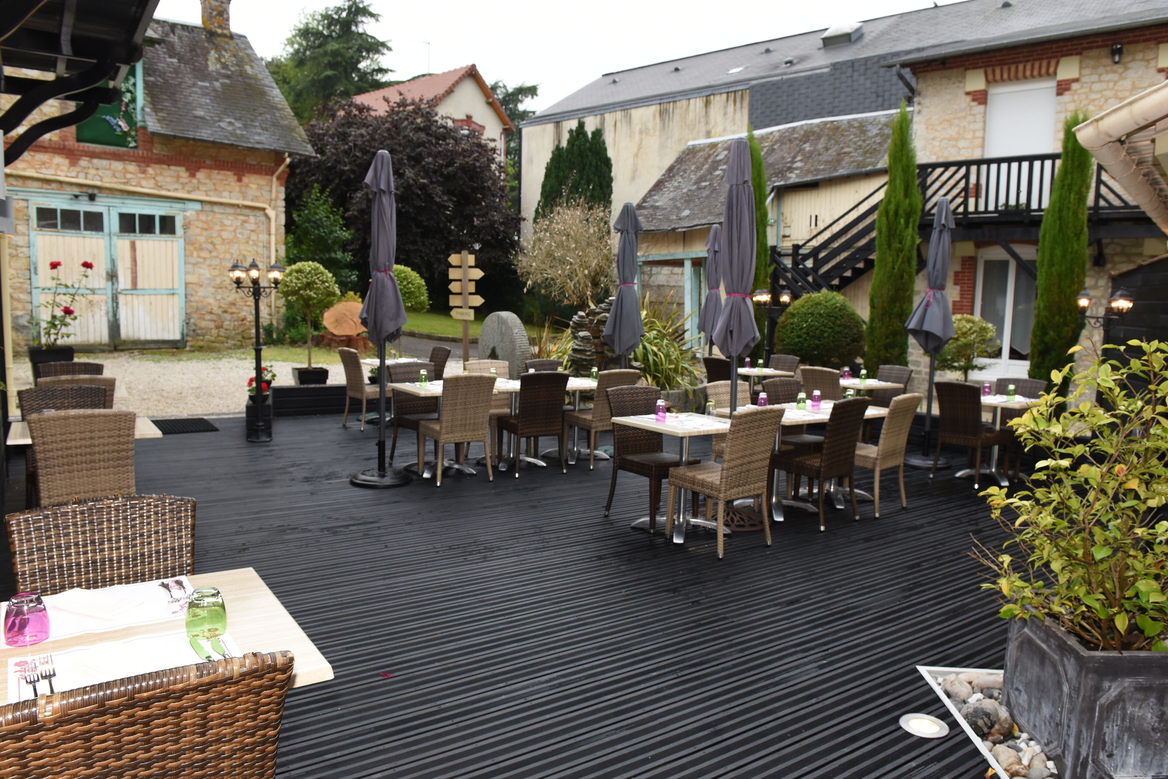 Une terrasse extérieure avec des meubles en osier, des parasols et un bâtiment en pierre en arrière-plan.
