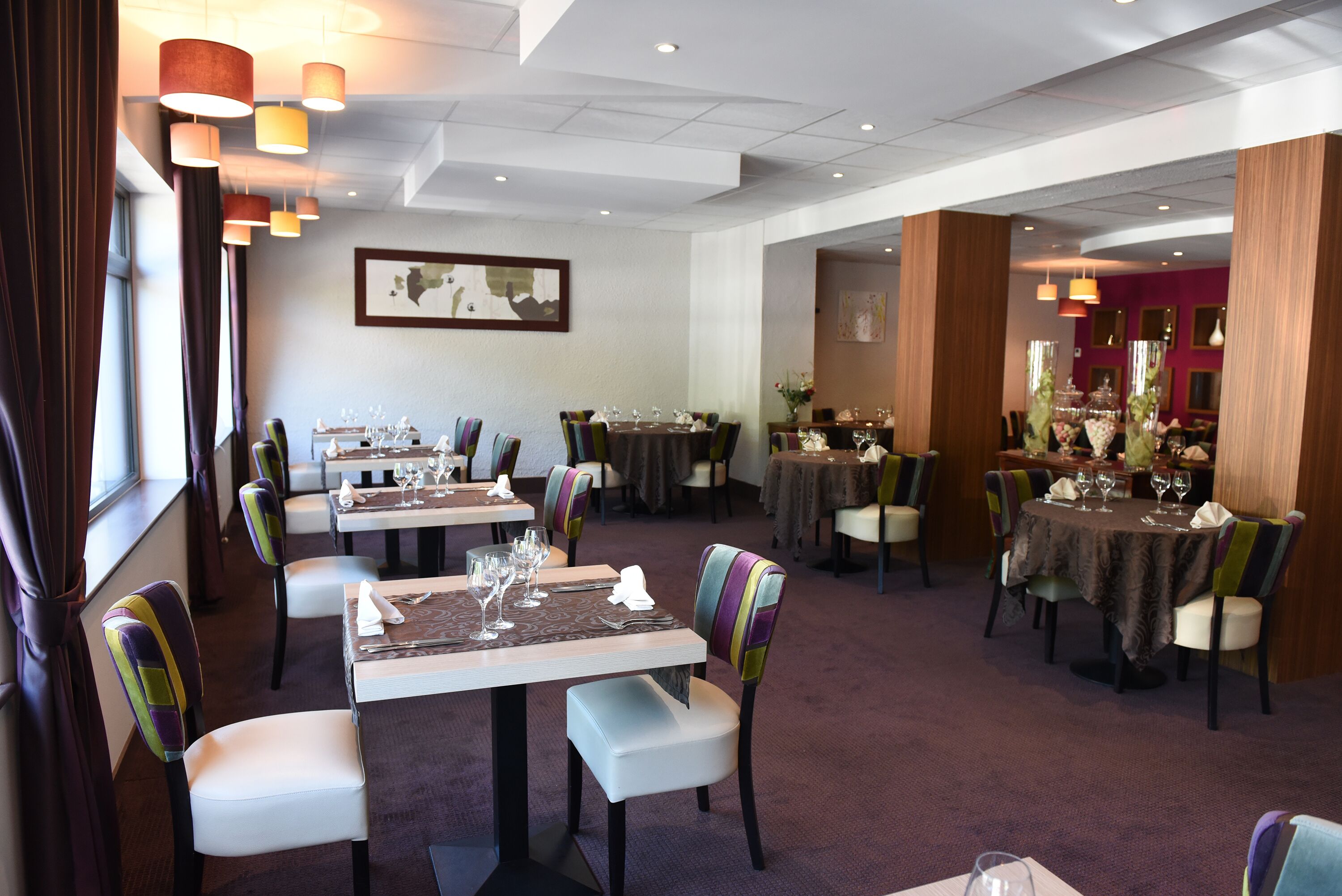 A restaurant with multiple dining tables and chairs, arranged in a spacious layout with pendant lighting.