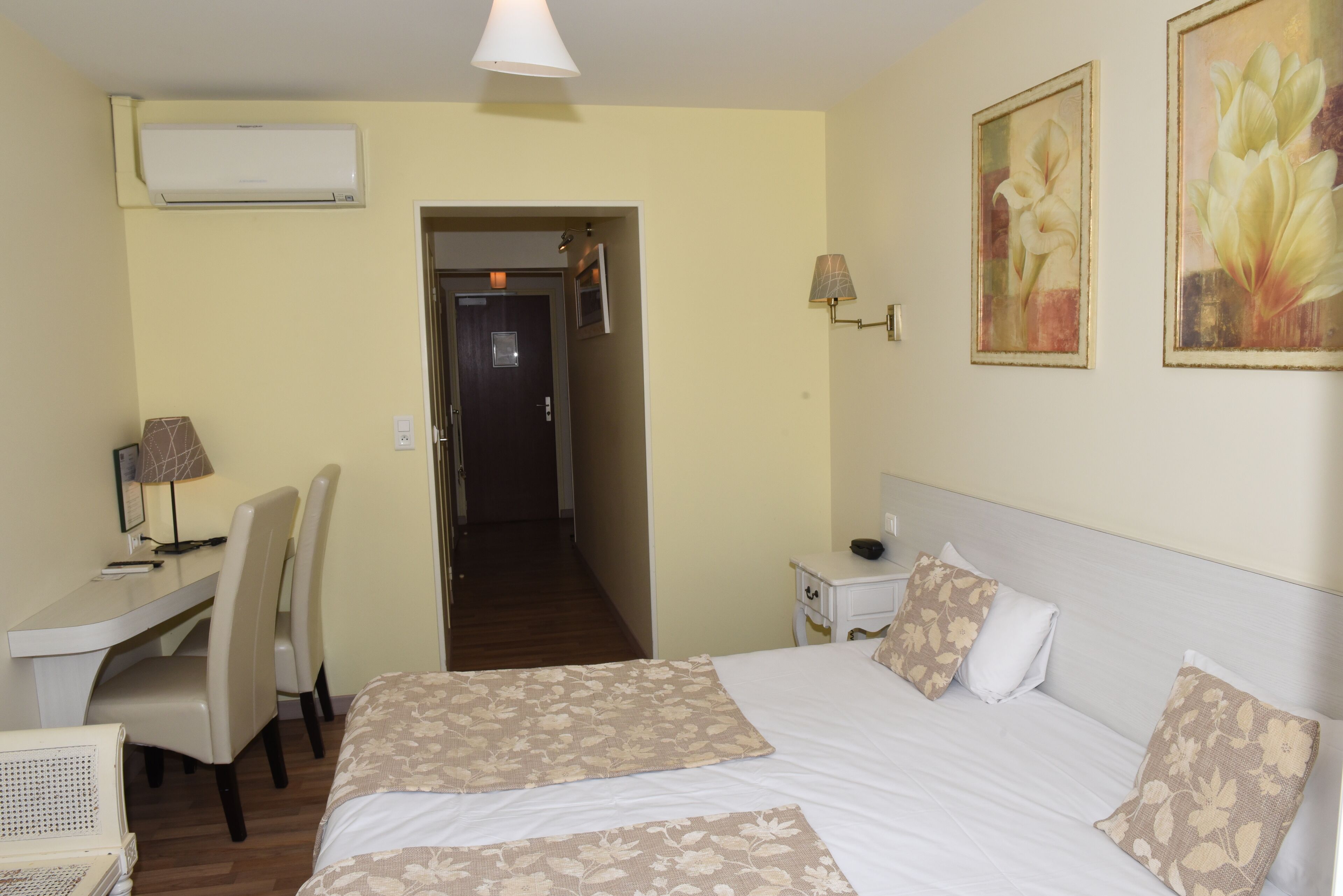 Una habitación de hotel con cama, escritorio, silla, lámpara y aire acondicionado instalado en la pared.
