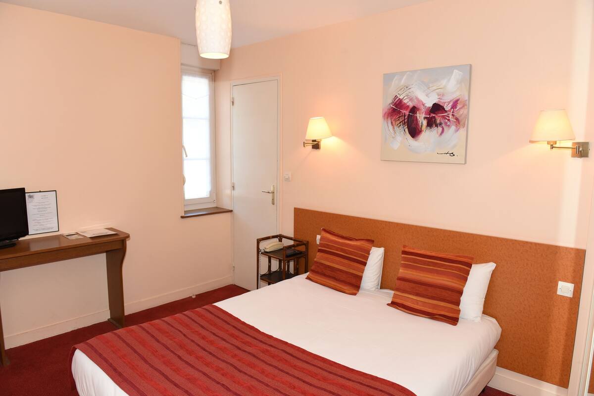 A hotel room with a bed, desk, and two wall-mounted lamps.