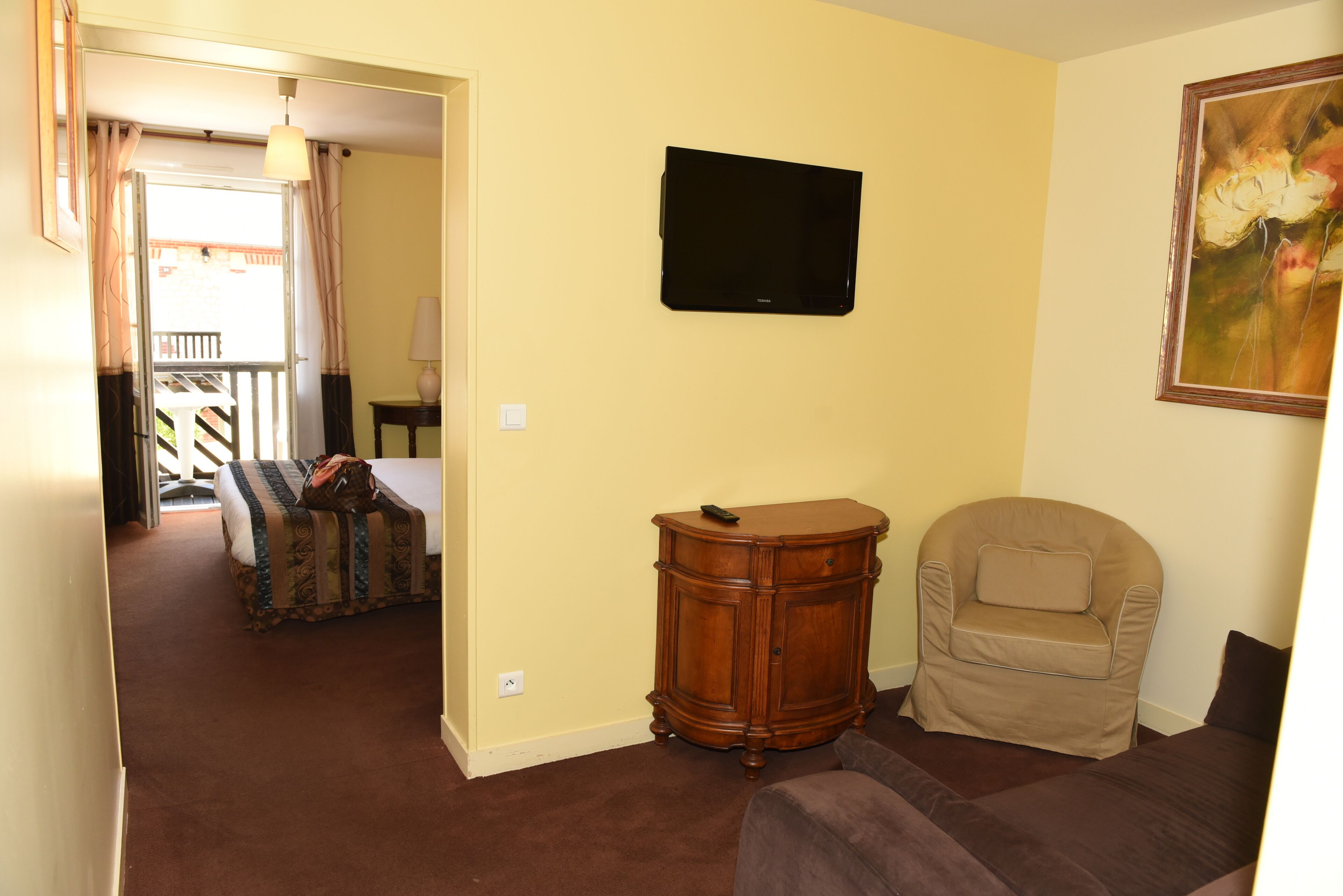 Una habitación con cama, una silla, un televisor y un cuadro.
