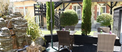 An outdoor patio with wicker furniture, a stone water feature, and a covered seating area.