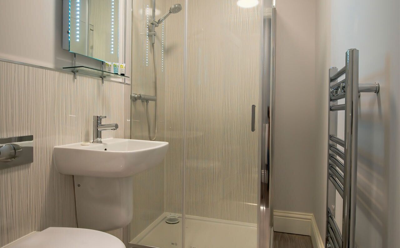 Un baño con cabina de ducha de vidrio, un lavabo blanco y un espejo con luces LED.