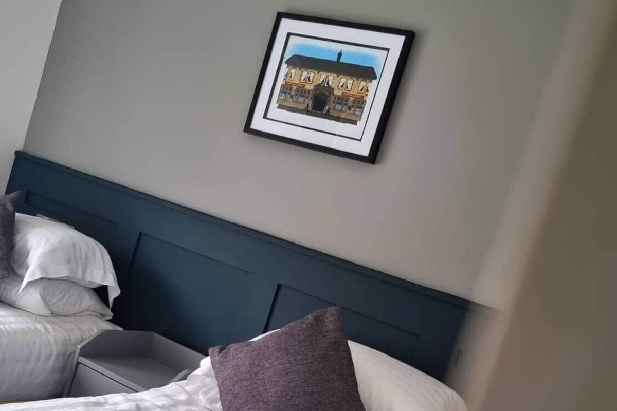 A hotel room with a bed, pillows, a headboard, and a framed picture on the wall.