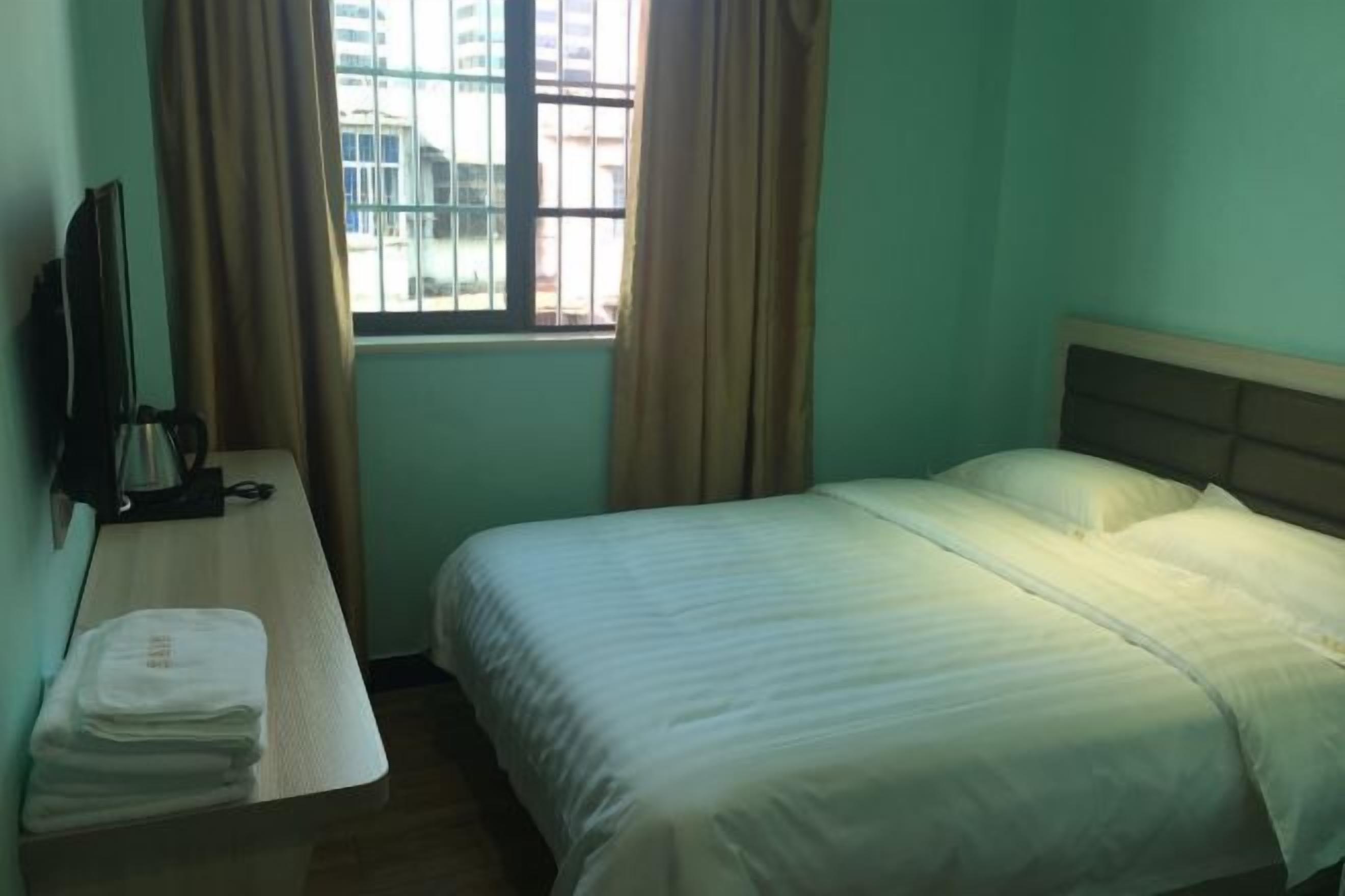 Quarto de hotel com uma cama, uma escrivaninha com cadeira, televisão e janela com cortinas.