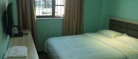 Quarto de hotel com uma cama, uma escrivaninha com cadeira, televisão e janela com cortinas.