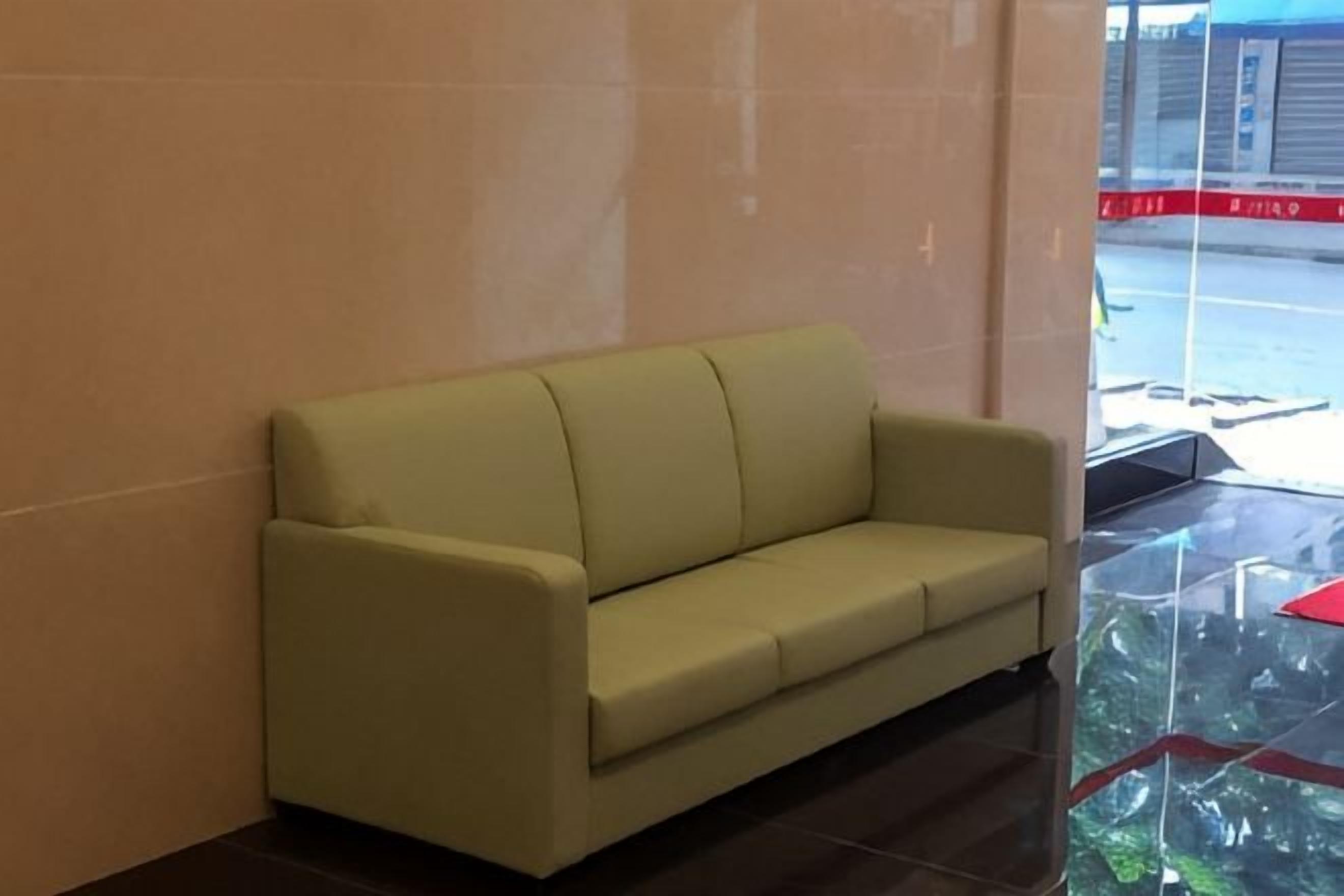 A plain, light-colored sofa against a wall with a reflective surface.