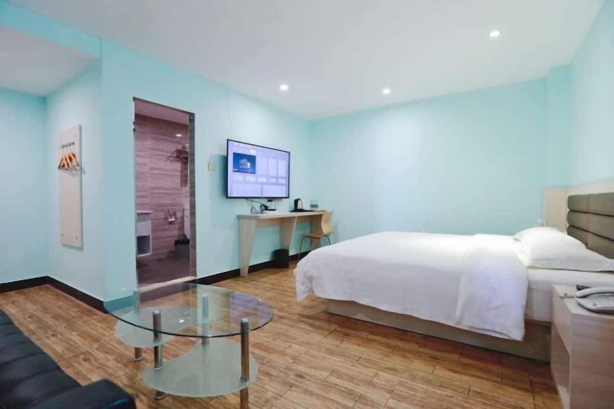 Une chambre d’hôtel comprenant un lit, un bureau, une table en verre, une télévision et une salle de bain visible à travers une porte en verre.