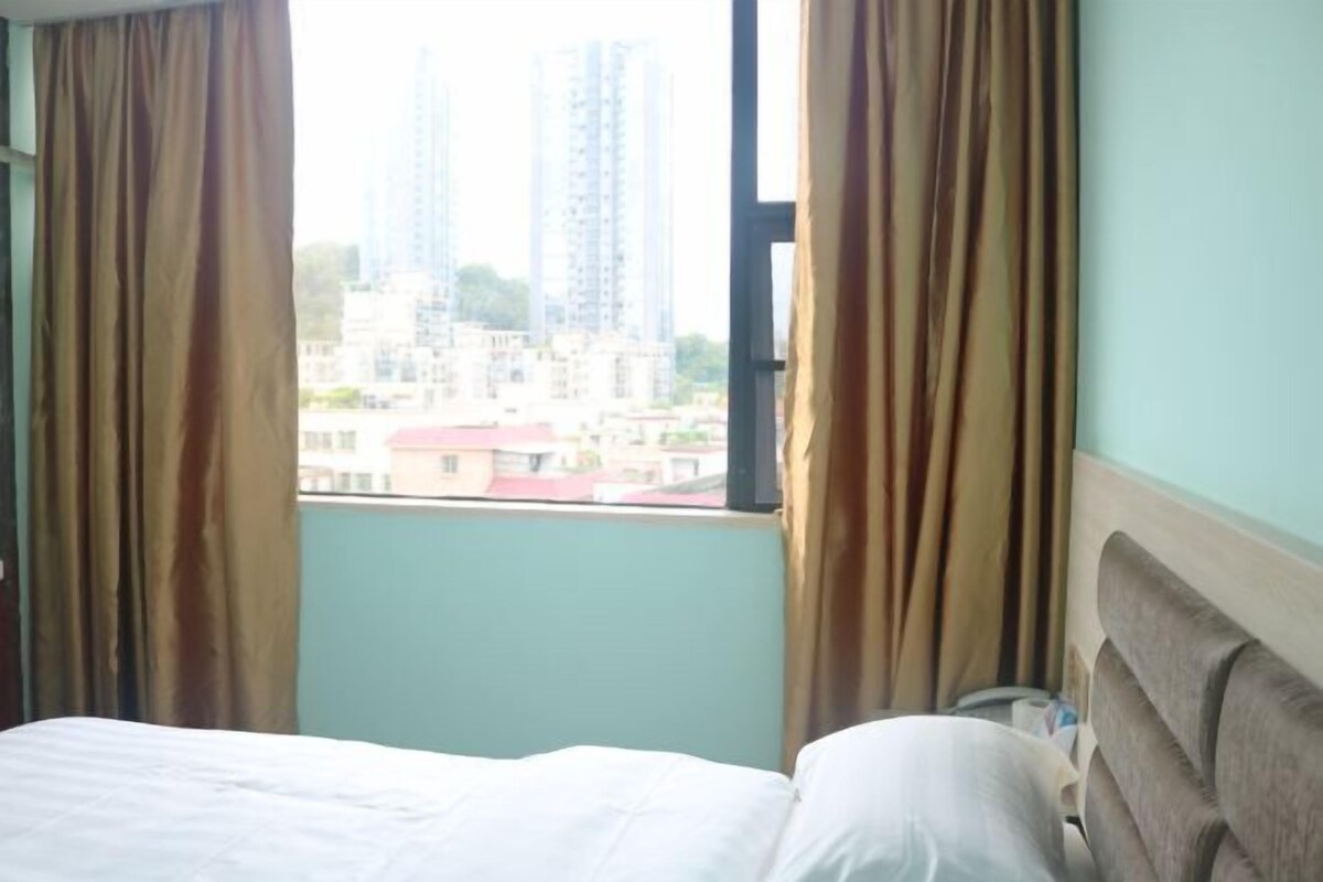 Een hotelkamer met een bed, gordijnen en een raam met uitzicht op gebouwen.