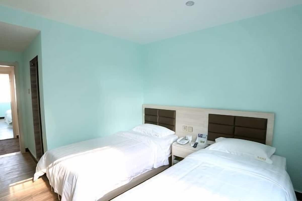 Une chambre d’hôtel avec deux lits, une tête de lit en bois, une table de chevet avec un téléphone et une porte donnant sur une autre chambre.