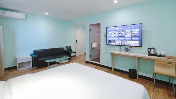 Ein Hotelzimmer mit Bett, einem an der Wand montierten Fernseher, der einen Film zeigt, einem Schreibtisch mit Stuhl und einem Sofa.