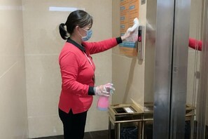 Iemand maakt een glazen liftdeur schoon met een spuitbus en een doek.