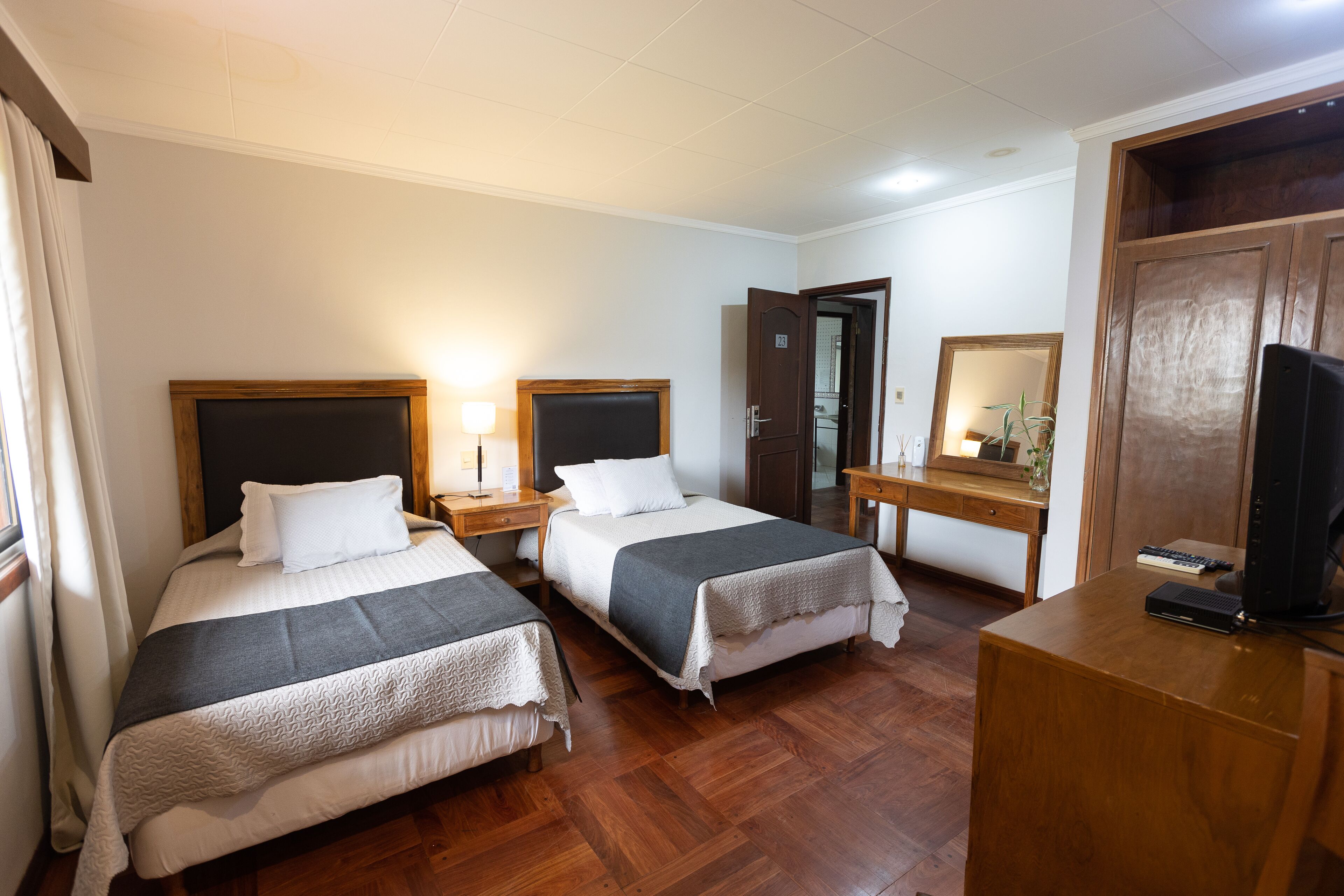 A hotel room with two beds, a desk, a chair, a television, and a mirror.